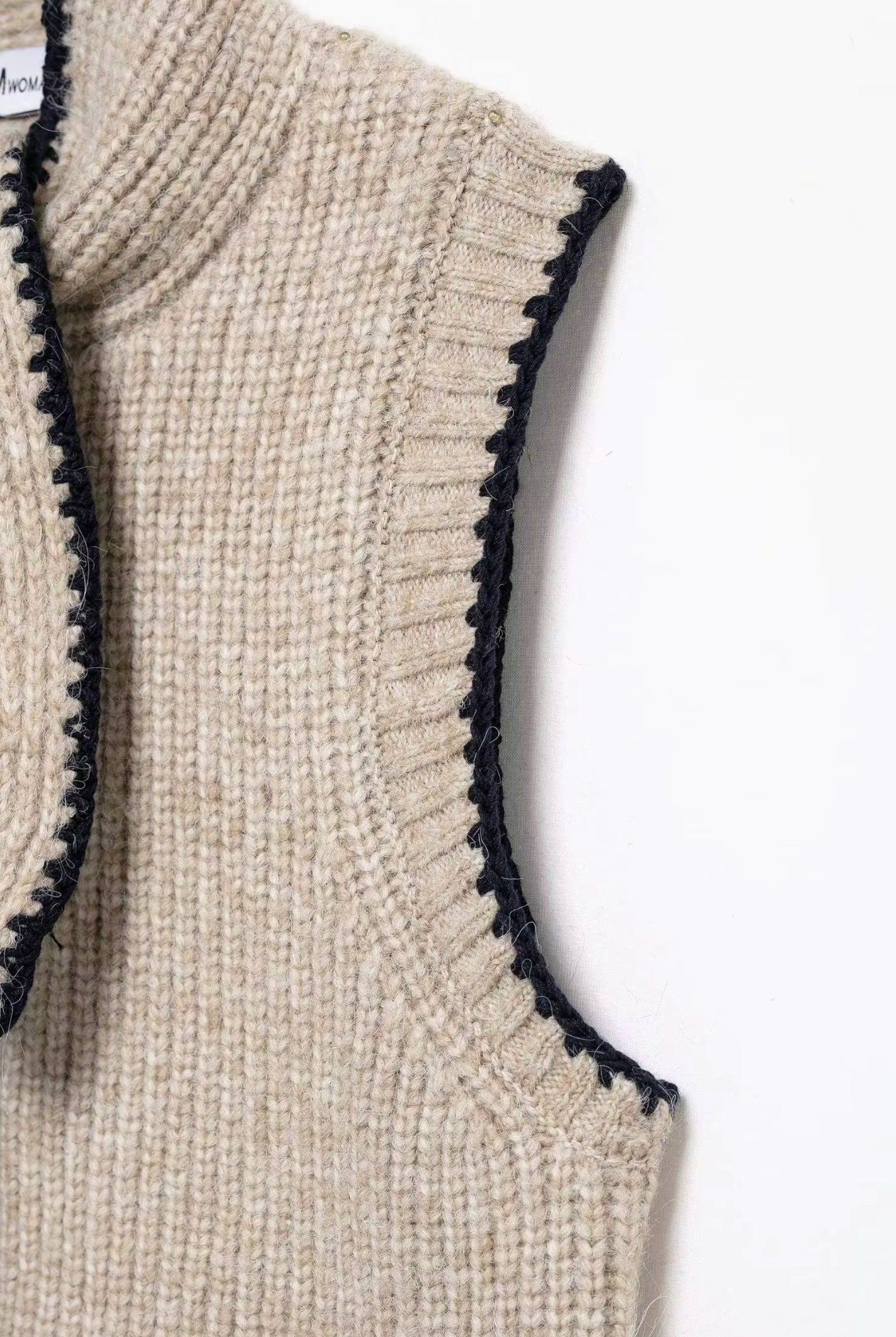 Close-up of a beige knitted vest with black trim on a white background