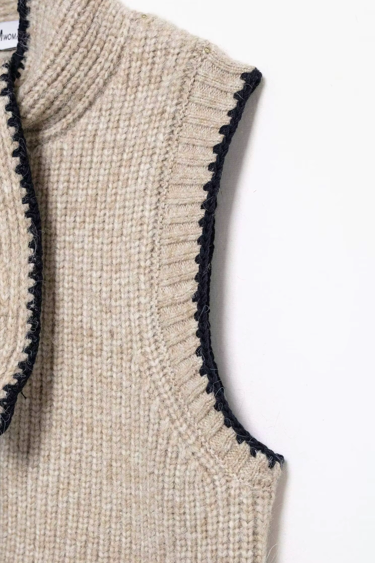Close-up of a beige knitted vest with black trim on a white background