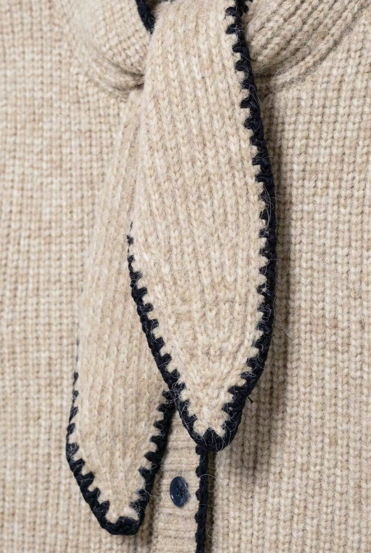 Close-up of a beige knitted garment with black trim on a beige background