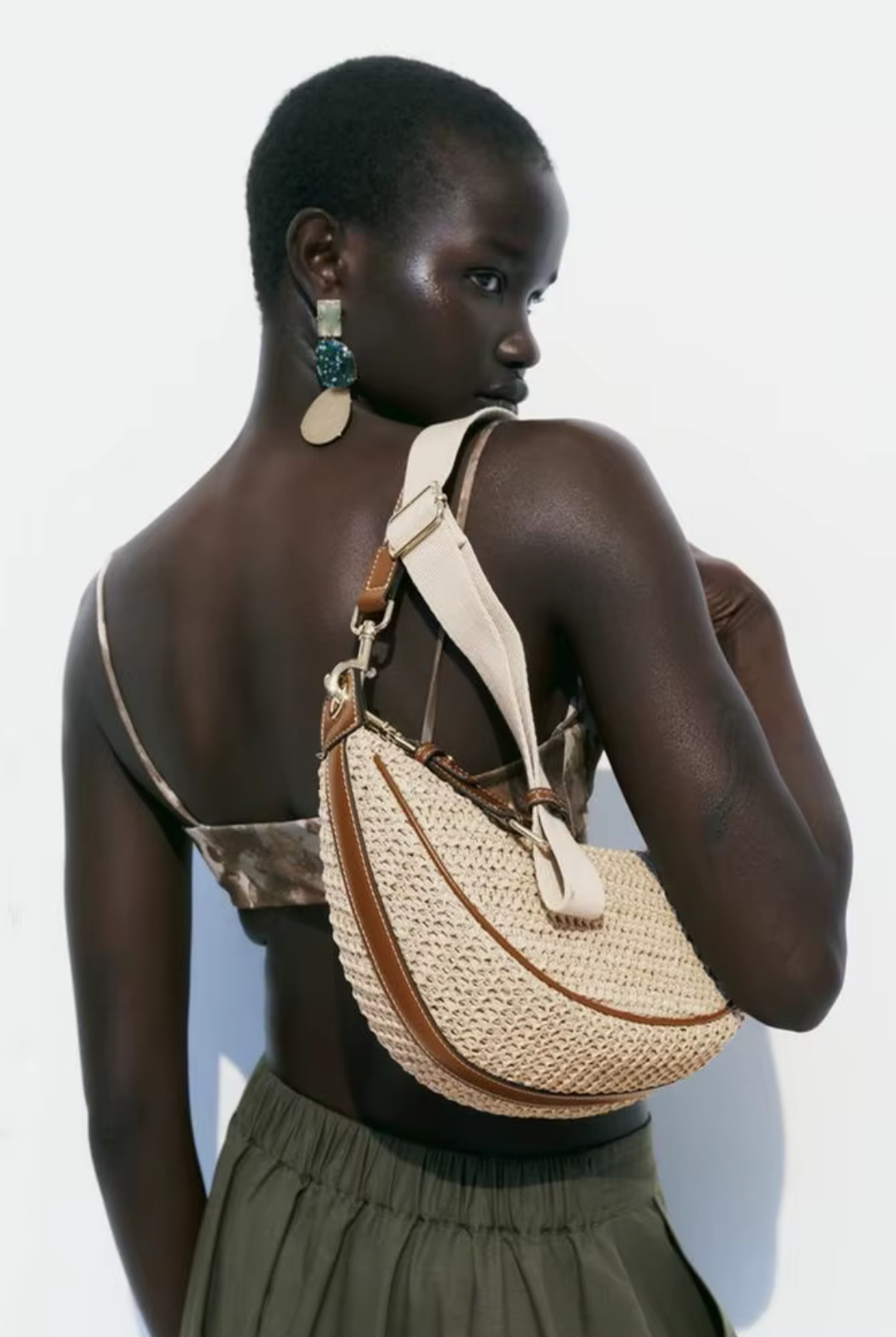 Woman carrying a woven handbag on a plain background