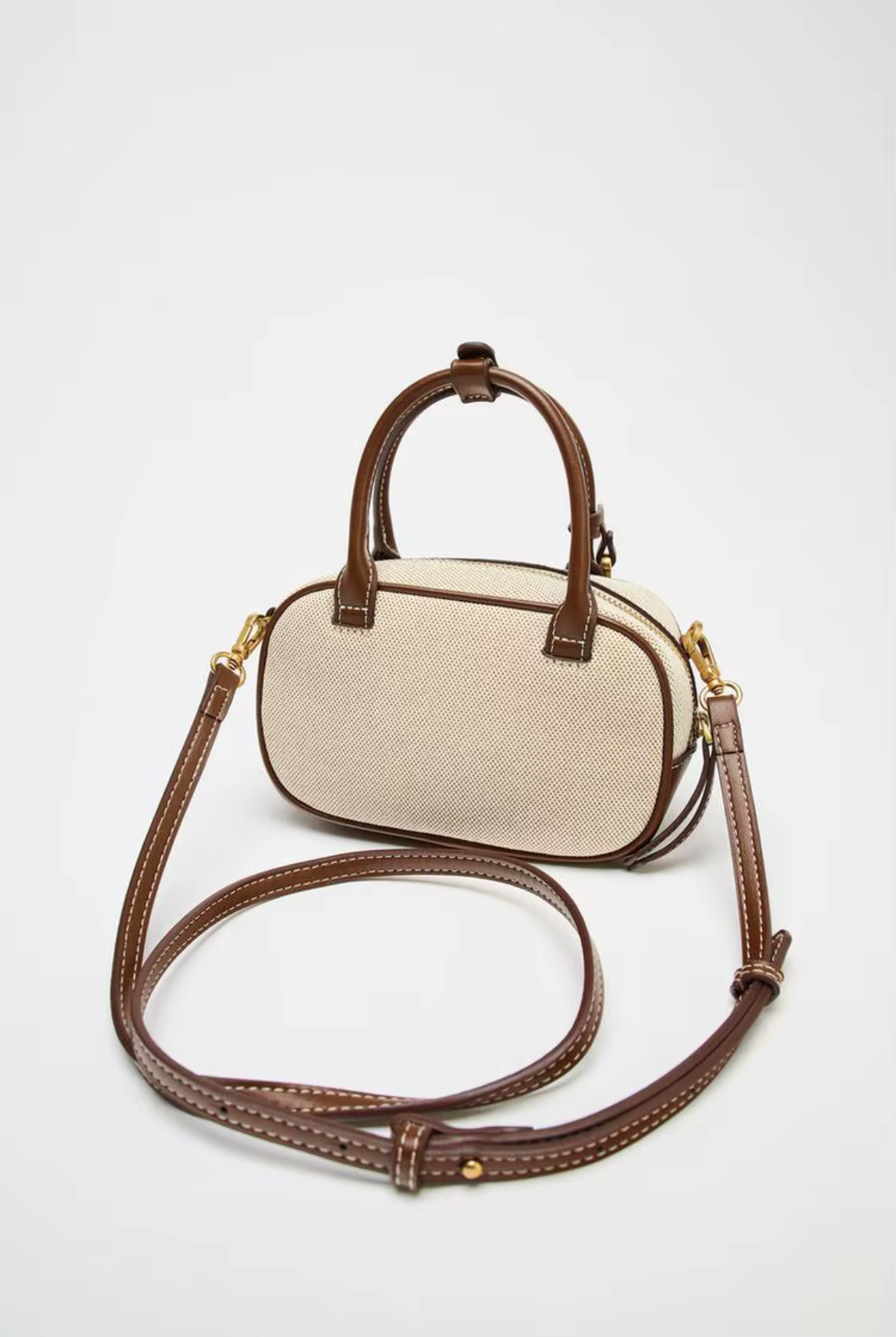 Beige handbag with brown handle and strap on a white background
