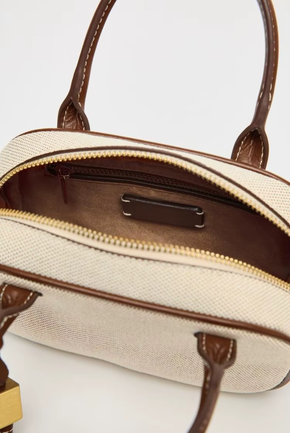 Close-up of a beige handbag with brown handles and trim on a white background