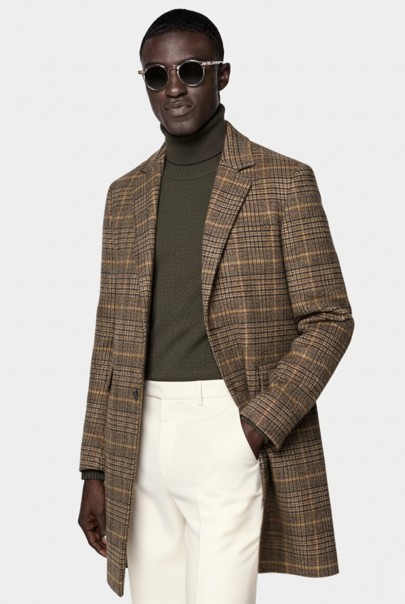 Man wearing a plaid overcoat, turtleneck, and white pants on a white background