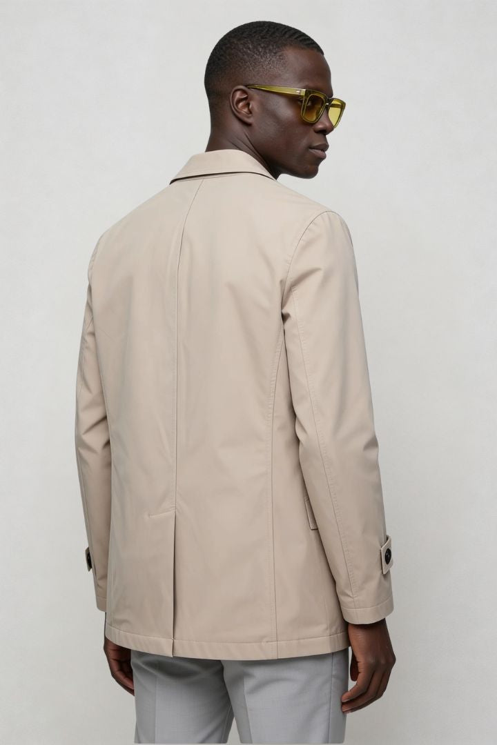 Man wearing a double-breasted beige trench coat with black buttons back view