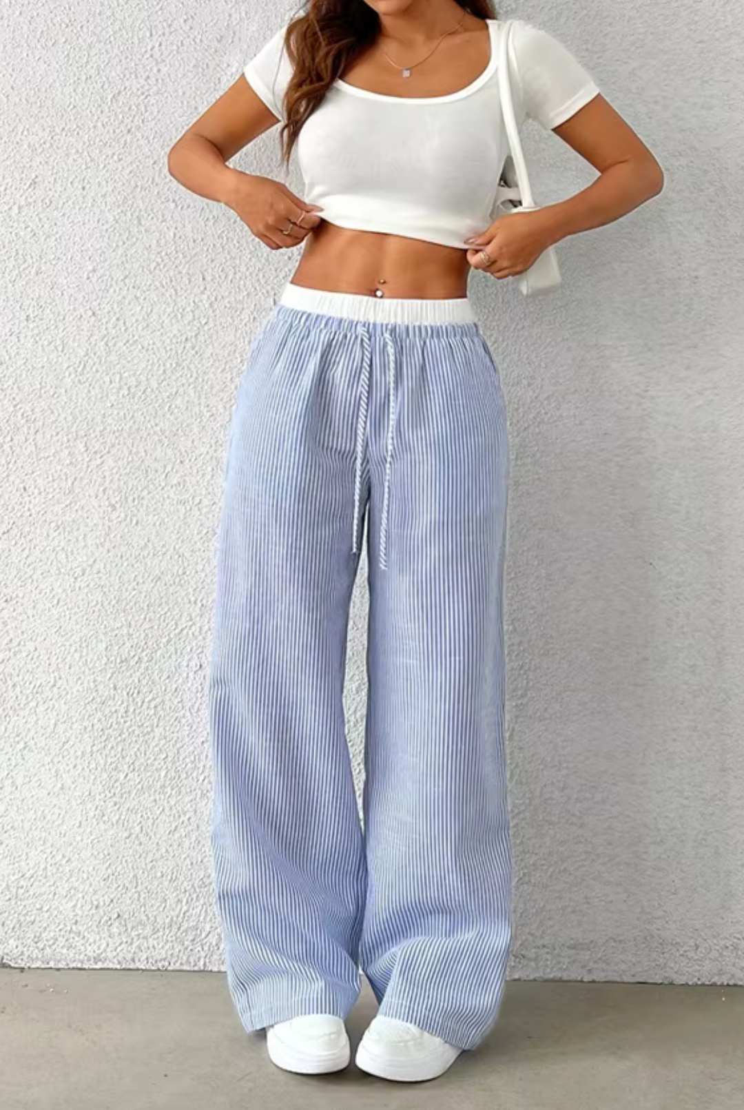 Person wearing a white crop top and blue striped pants against a plain background