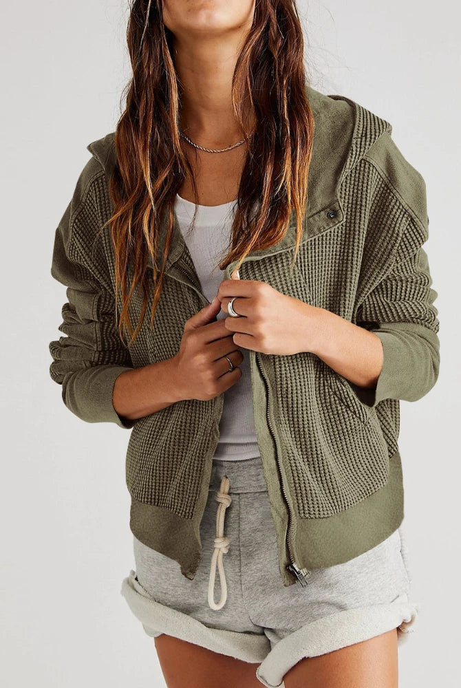 Person wearing a green textured jacket over a white top and gray shorts on a white background