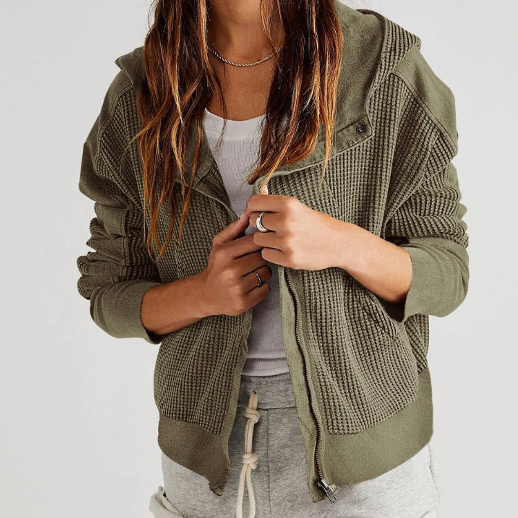 Person wearing a green textured jacket over a white top and gray shorts on a white background