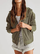 Person wearing a green textured jacket over a white top and gray shorts on a white background