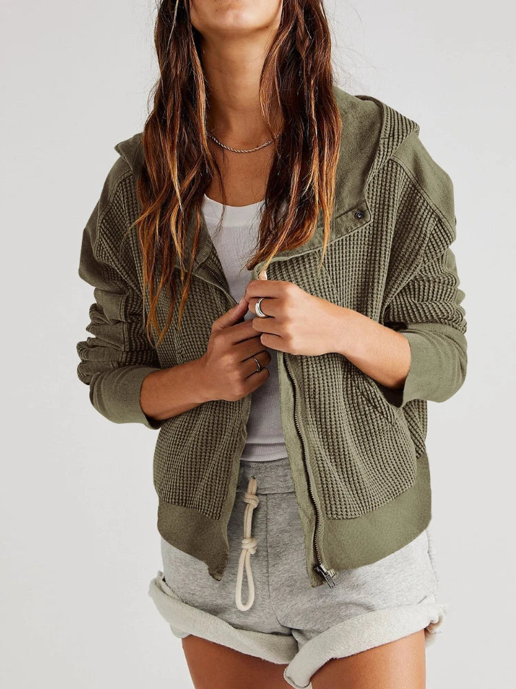 Person wearing a green textured jacket over a white top and gray shorts on a white background