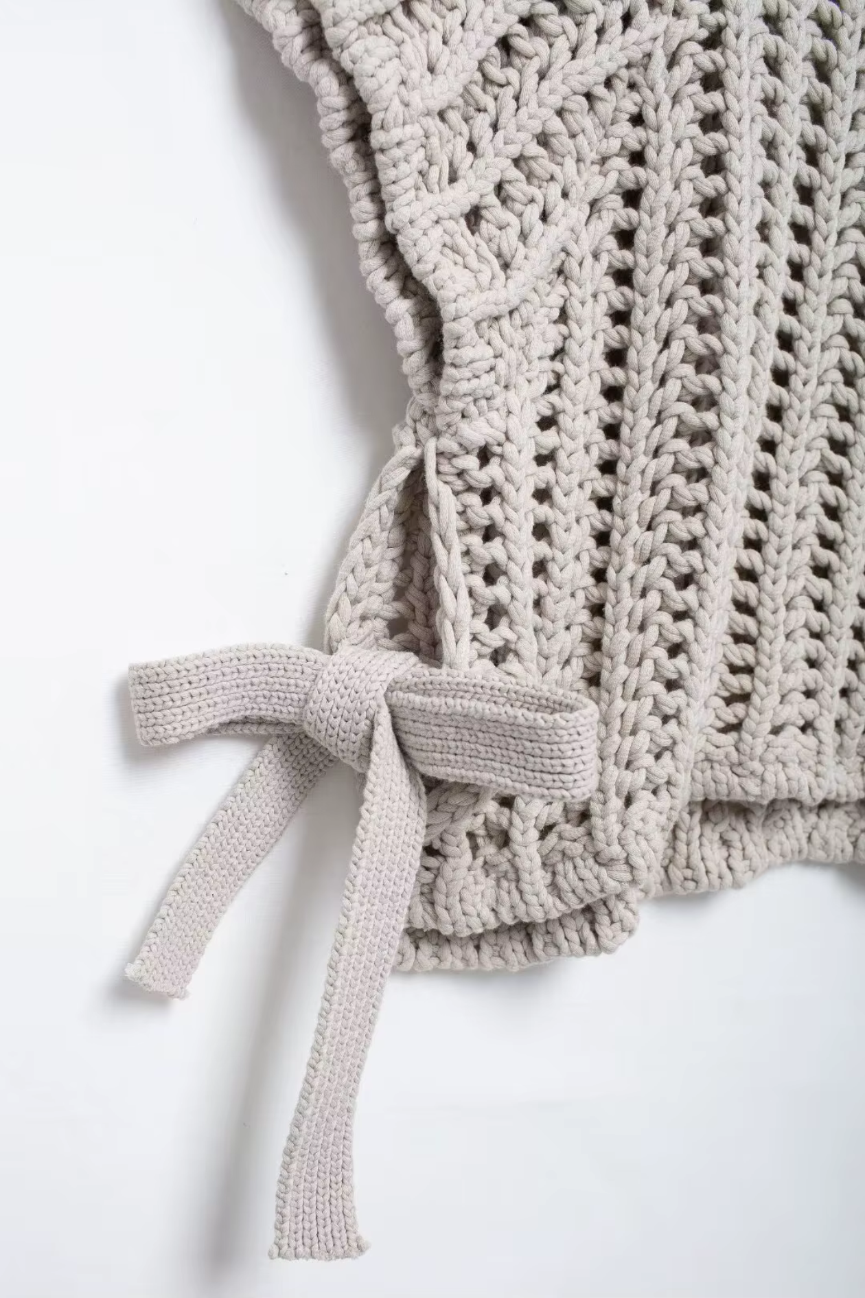 Close-up of a beige crochet vest with a bow on a white background