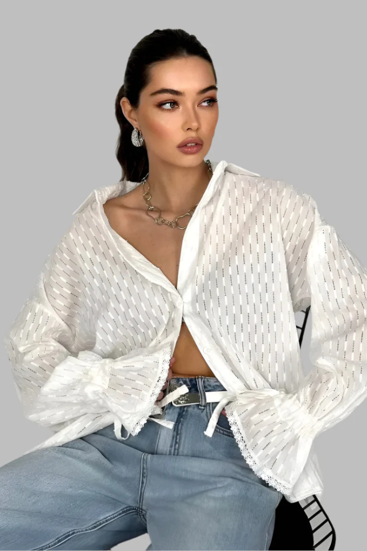 Woman wearing a white textured cardigan over a black top with blue jeans on a gray background