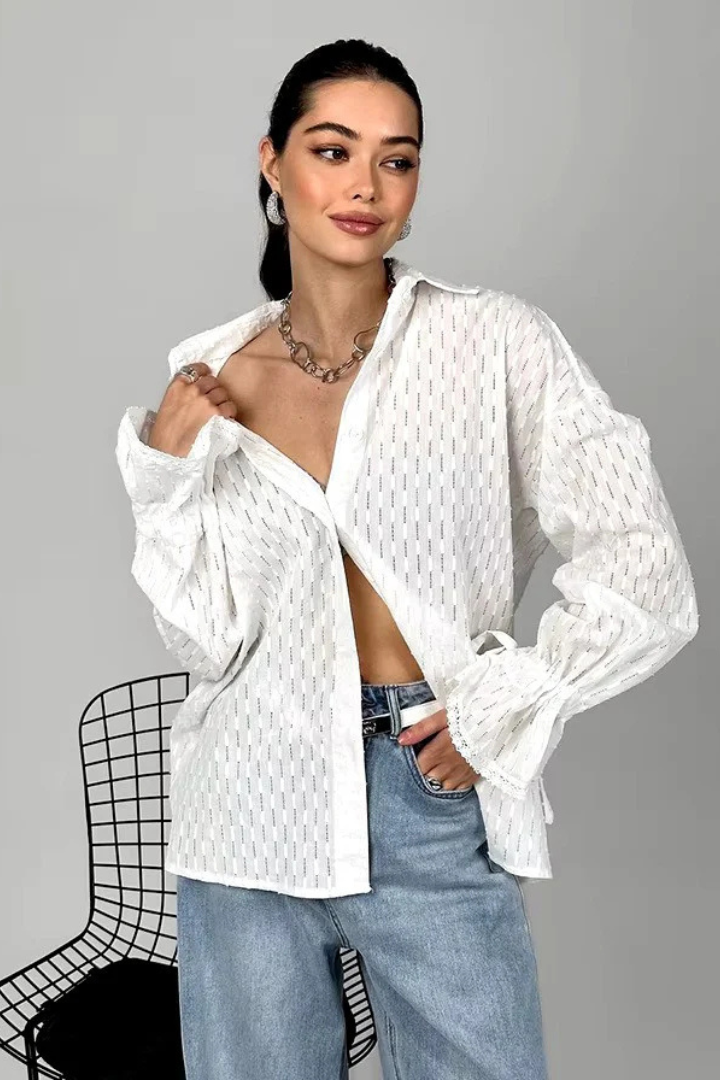 Woman wearing a white textured shirt with rolled-up sleeves and blue jeans on a gray background