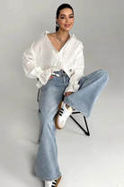Woman sitting on a chair wearing a white blouse, blue jeans, and white sneakers.