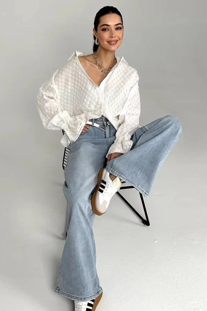 Woman sitting on a chair wearing a white blouse, blue jeans, and white sneakers.