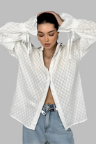 Person wearing a white textured shirt over a black top with light blue jeans on a gray background