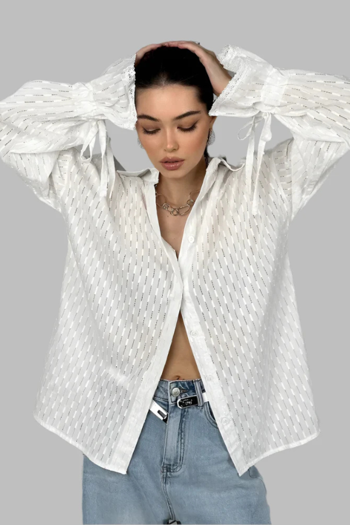 Person wearing a white textured shirt over a black top with light blue jeans on a gray background
