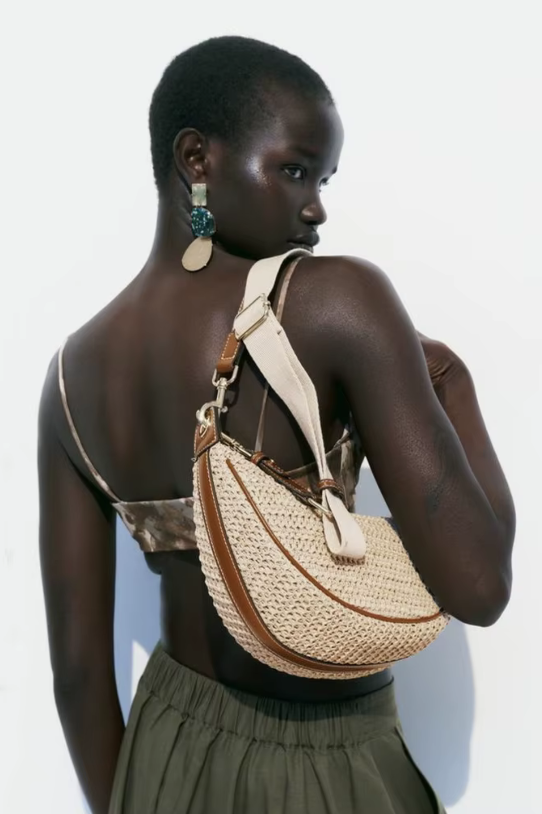 Woman carrying a woven handbag on a plain background