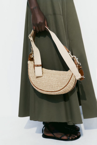 Person holding a woven handbag with a plain background