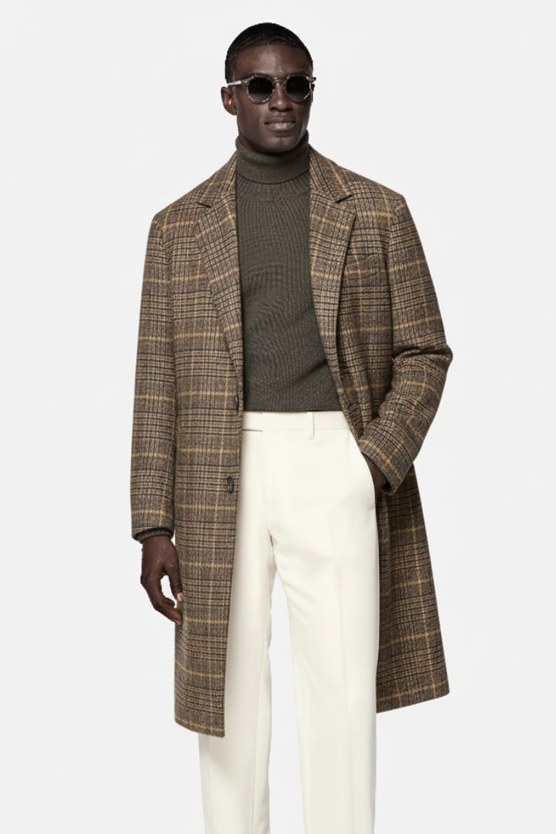 Man wearing a plaid coat, green sweater, and white pants on a light gray background
