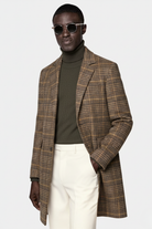 Man wearing a plaid overcoat, turtleneck, and white pants on a white background