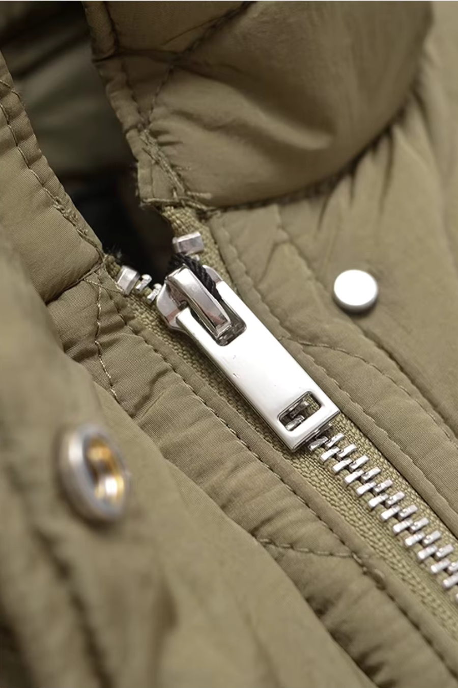 Close-up of silver zipper and snap placket on olive quilted puffer jacket