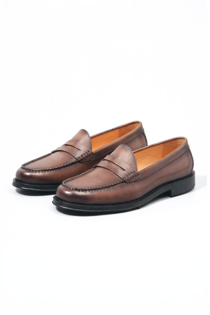 Premium men’s leather penny loafers with classic slip-on silhouette and refined stitching detail in brown