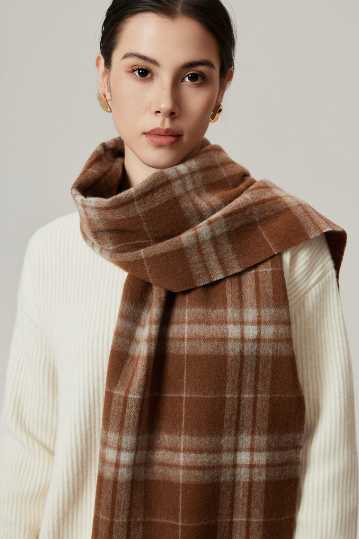 Woman wearing a brown plaid scarf over a white sweater on a neutral background