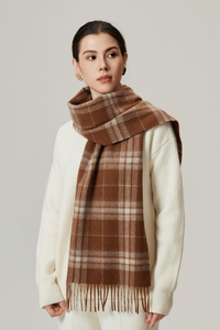 Woman wearing a brown plaid scarf and white sweater on a plain background