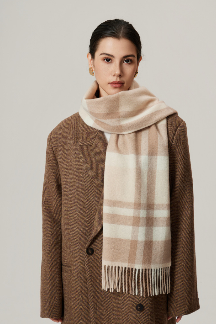 Woman wearing a brown coat and beige checkered scarf against a plain background