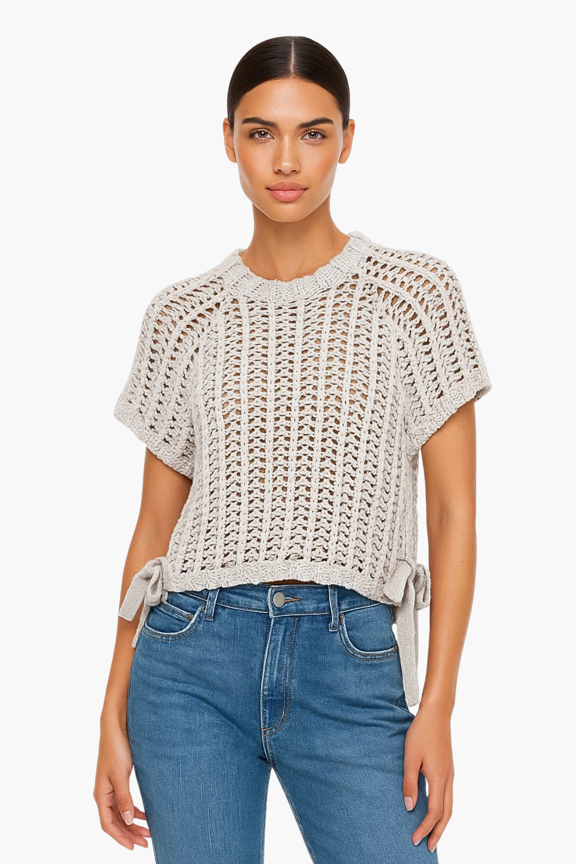 Woman wearing a beige knitted top and blue jeans on a white background
