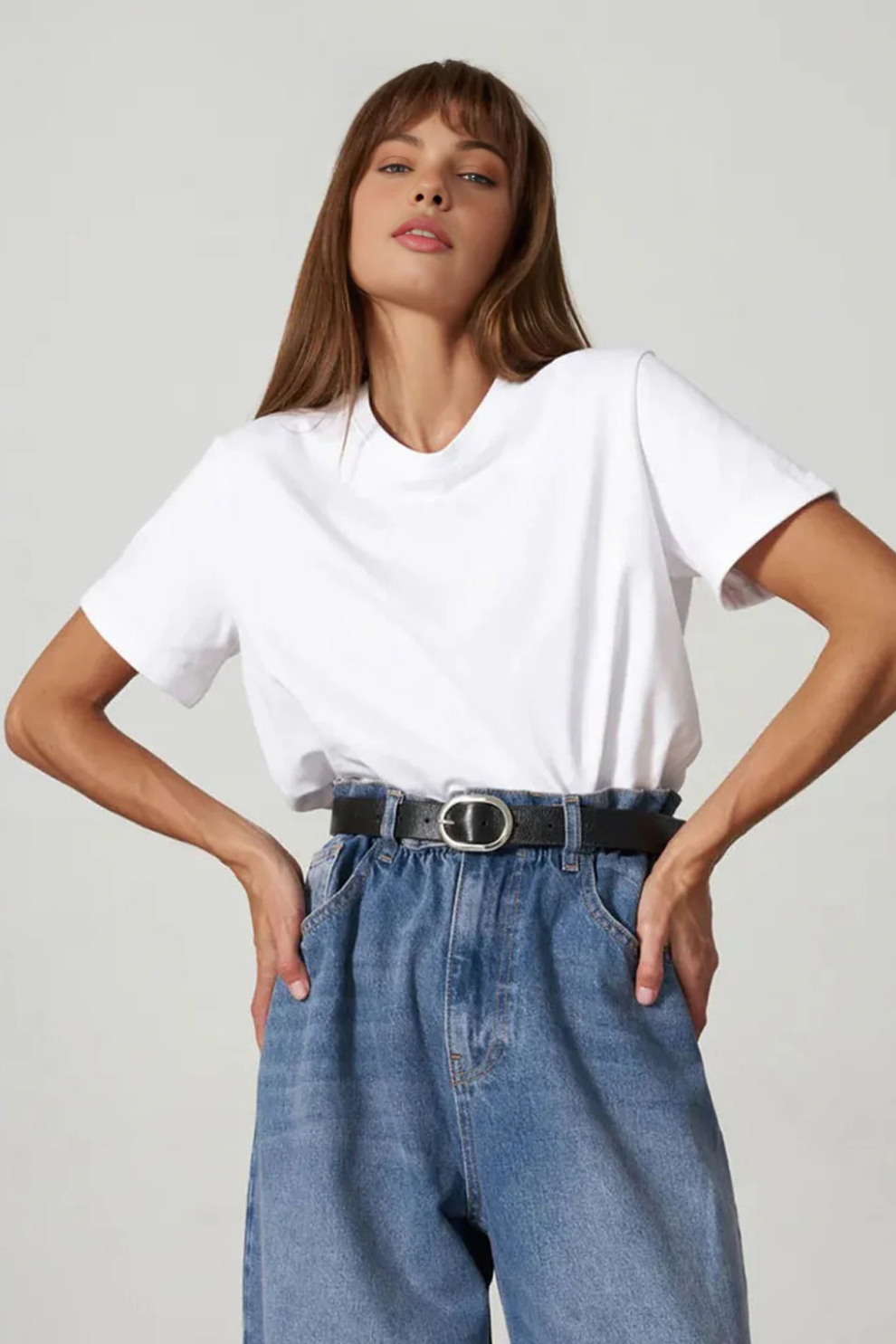 Woman wearing a white t-shirt and blue jeans on a plain background