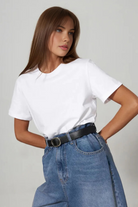 Woman wearing a white t-shirt and blue jeans against a plain background